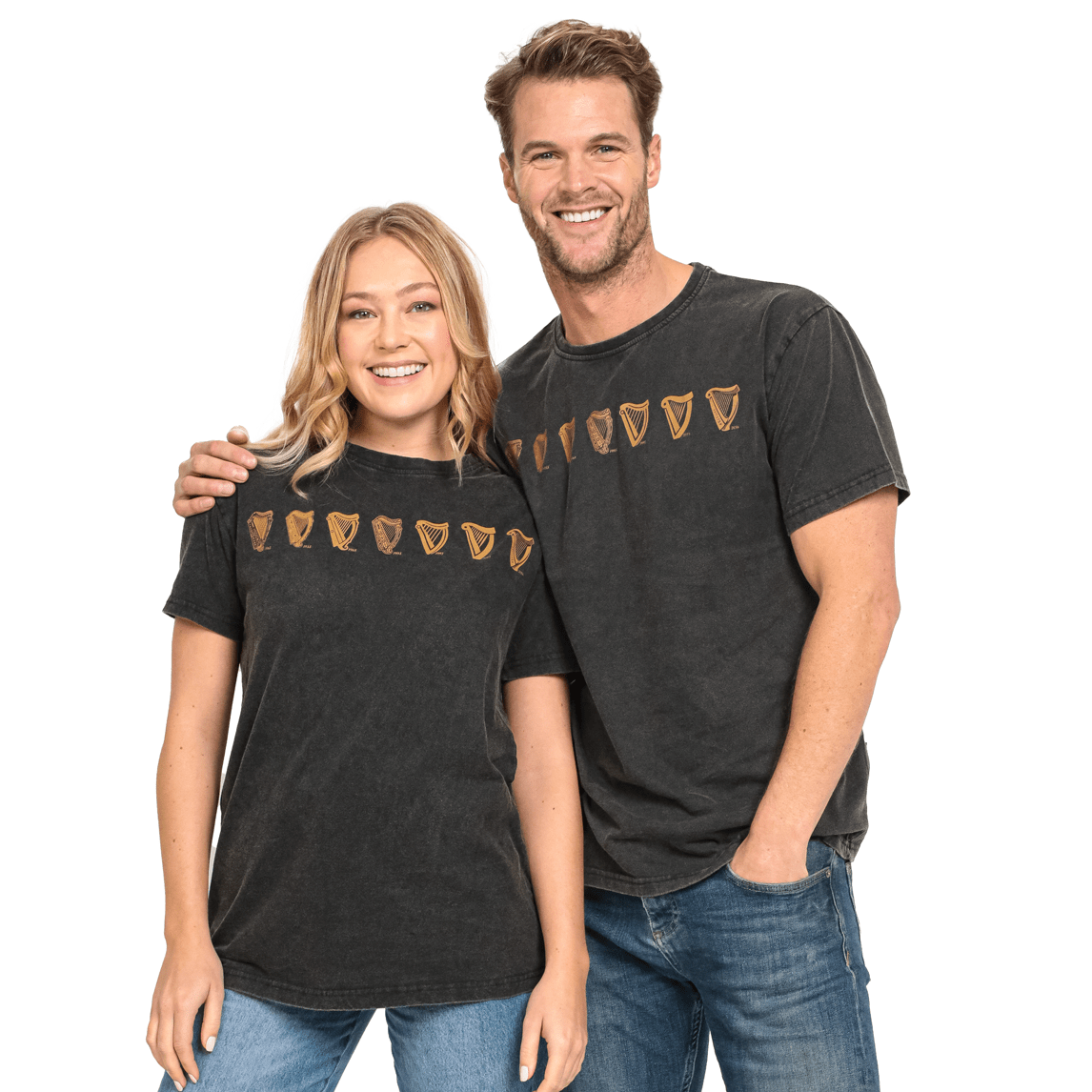 A smiling woman and man wearing matching Guinness Black Evolution Harp Premium Tee 100% cotton black t-shirts with golden shield-like patterns, standing closely together, casual in jeans.