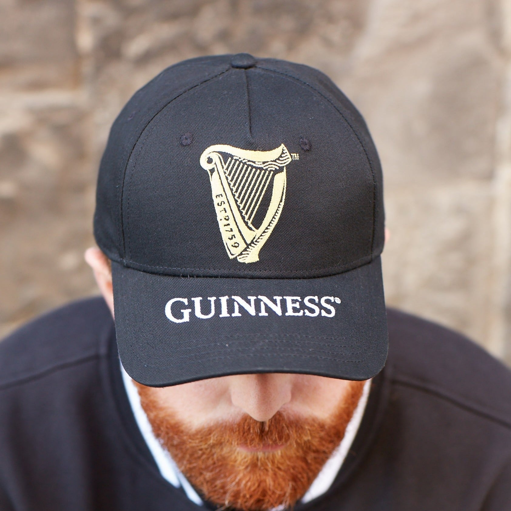 A man with a red beard wearing a Guinness hat and a Guinness Harp Baseball Cap made of cotton.