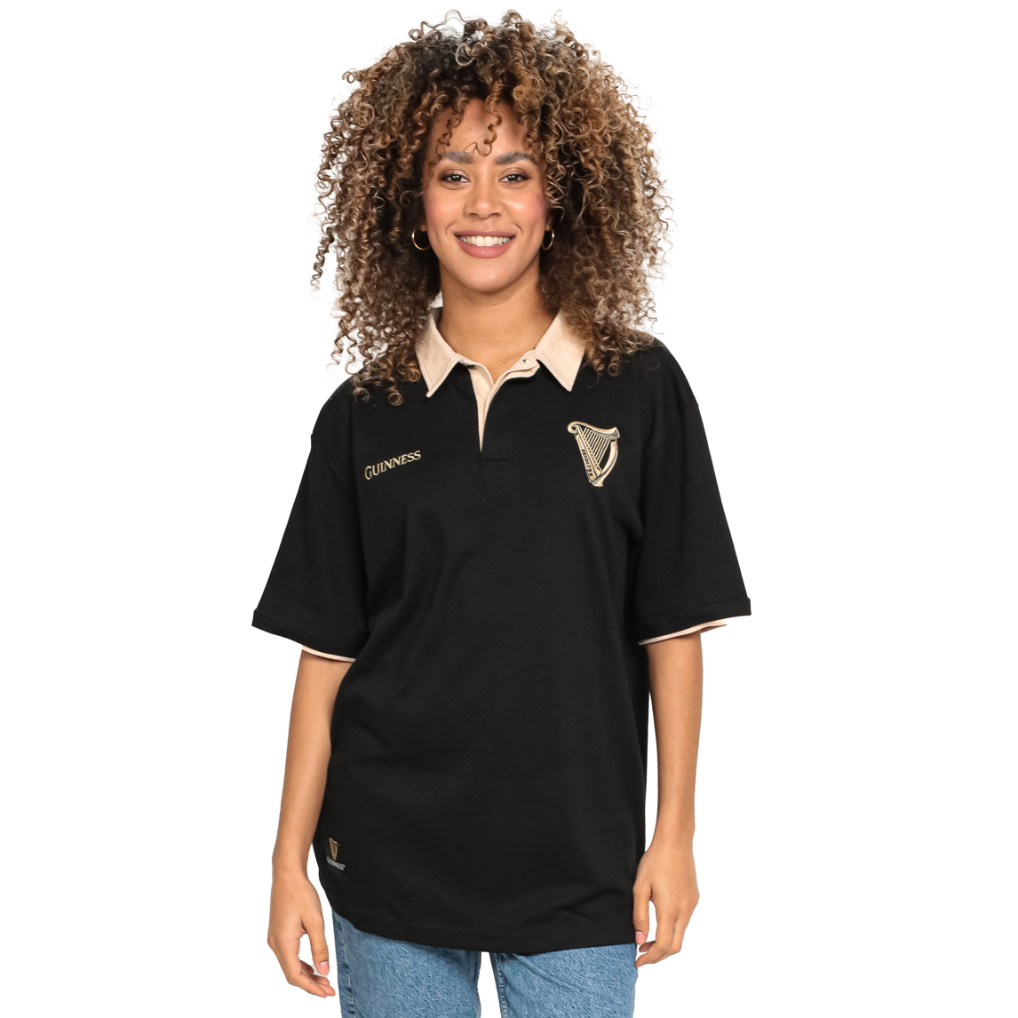 A person with curly hair wears a Black and Cream Traditional Short Sleeve Rugby by Guinness and blue jeans against a white background, showcasing the style of a true sports lover.