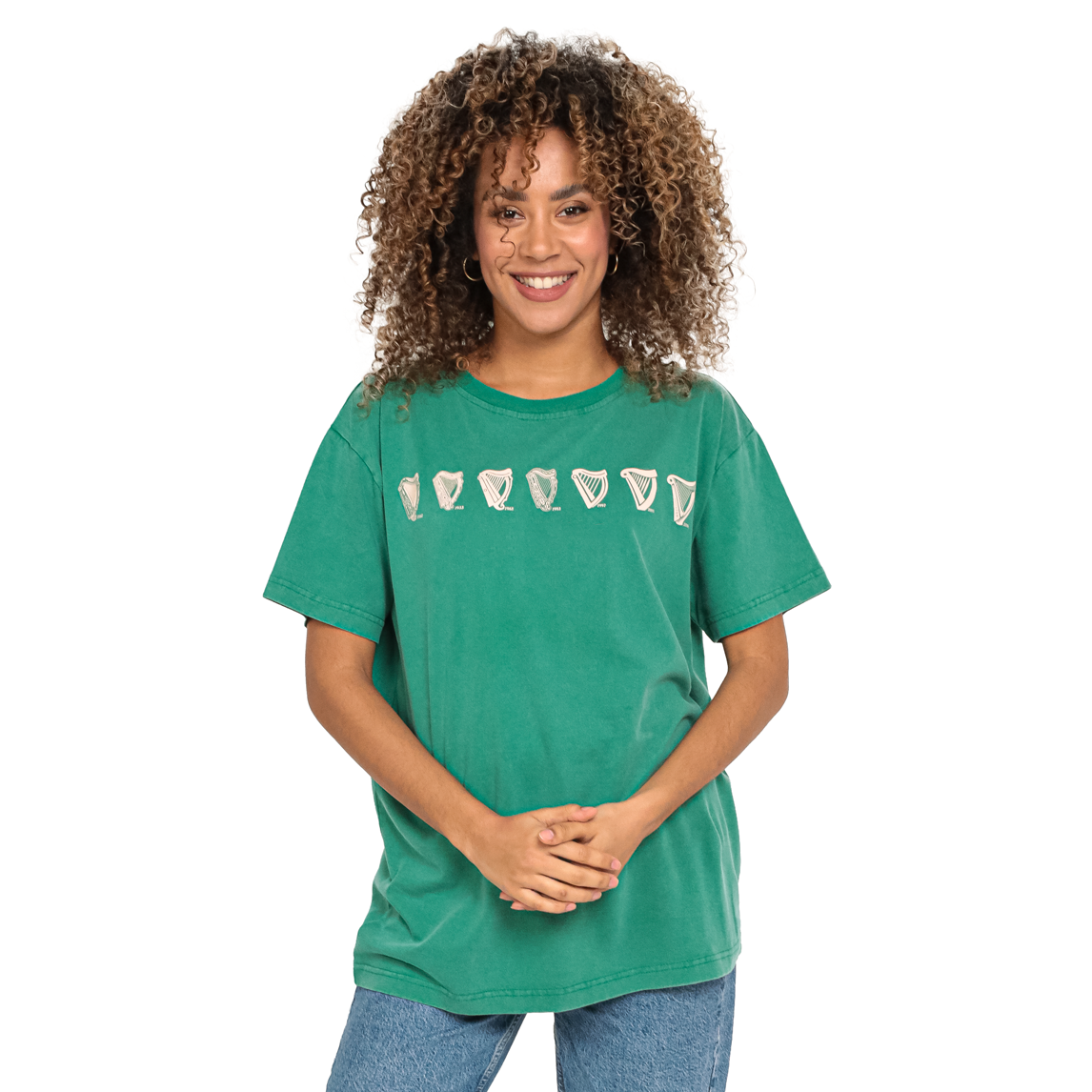 A person with curly hair smiles, donning the Green Evolution Harp Premium Tee by Guinness.