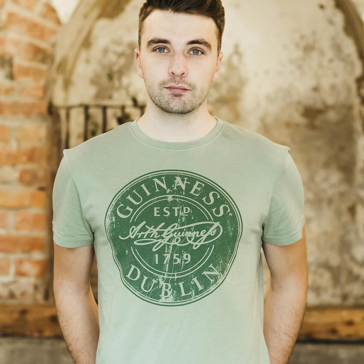 A man wearing a Guinness Green Bottle Cap Tee that says Guinness.