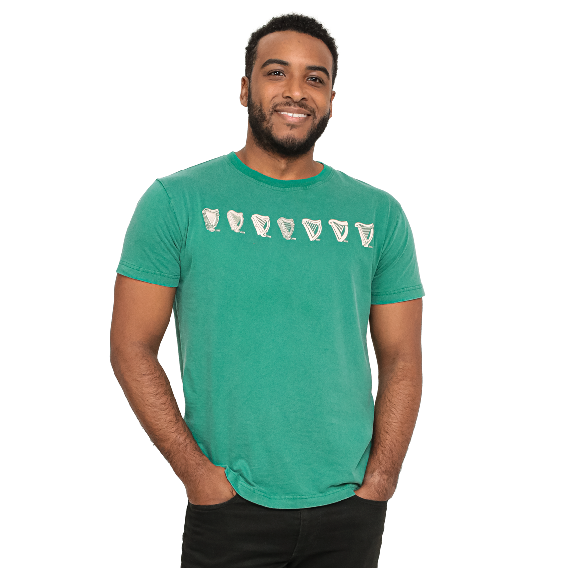 A man in a green t-shirt with seven white outlined shapes across the chest, hands in pockets, and smiling at the camera. The shirt proudly displays the Green Evolution Harp Premium Tee by Guinness.