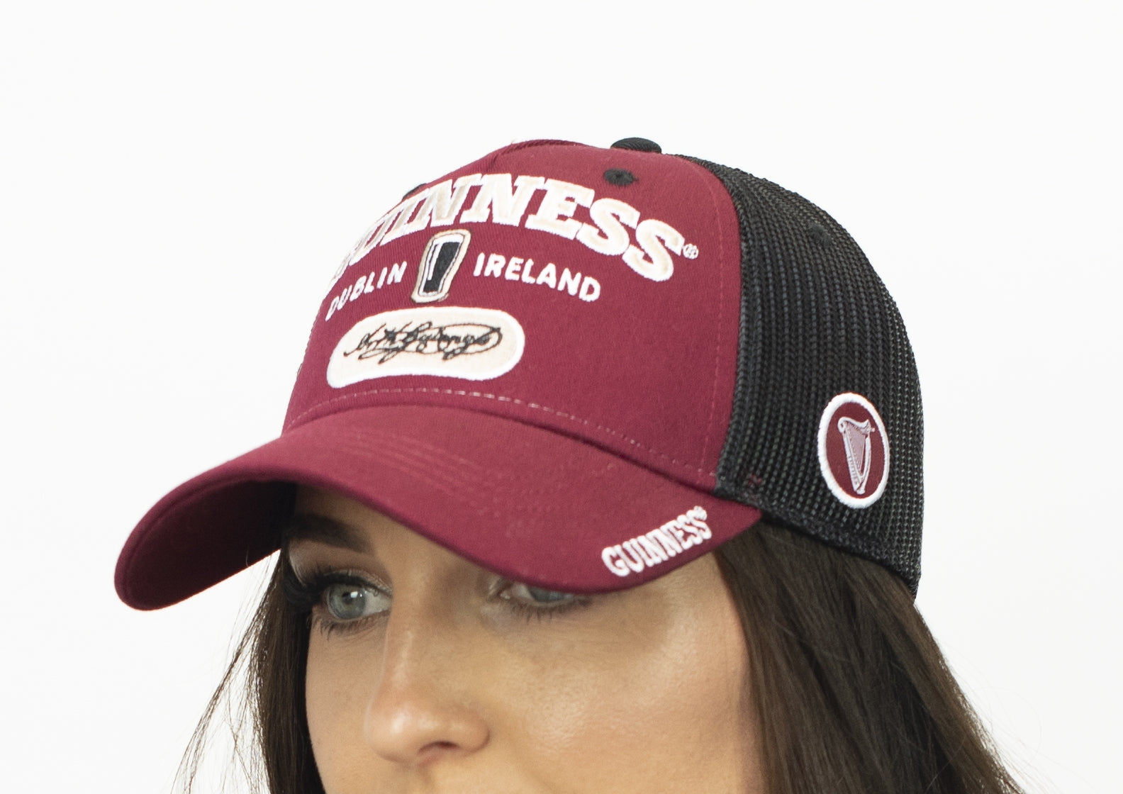 A woman wearing a Guinness Signature Burgundy Trucker Mesh Baseball Cap Adjustable.