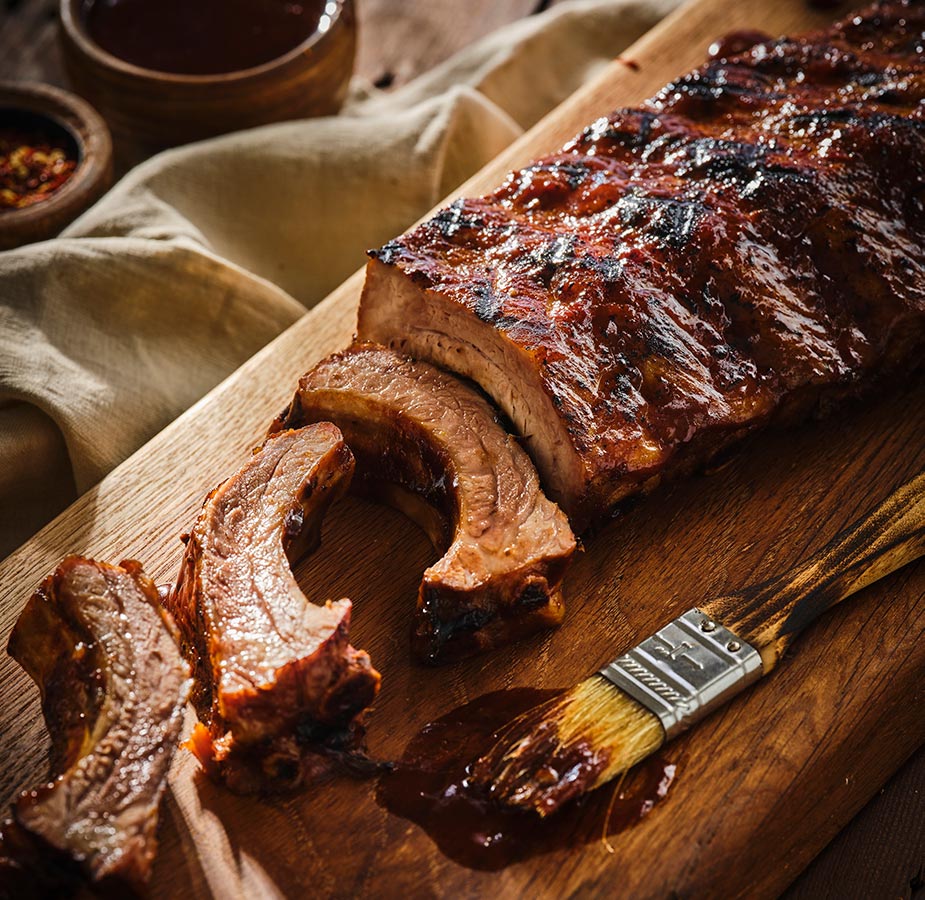 Bbq ribs with Guinness Smokey Marinade Sauce on a wooden cutting board.