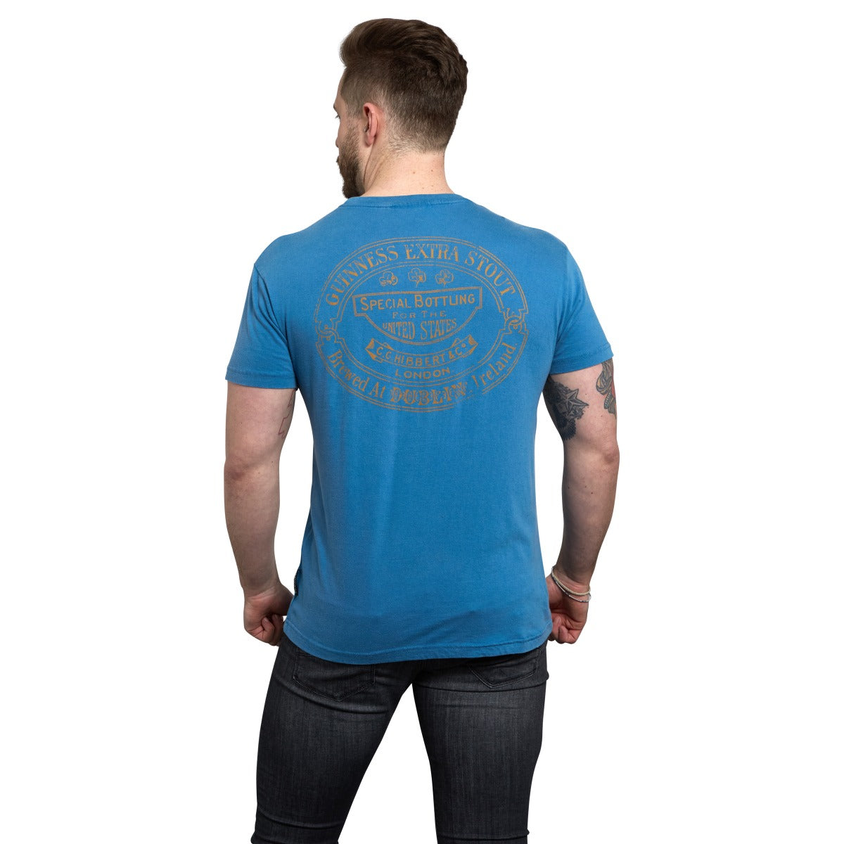 Man standing with his back to the camera, wearing a blue Guinness Blue Harp Premium Tee and dark jeans.