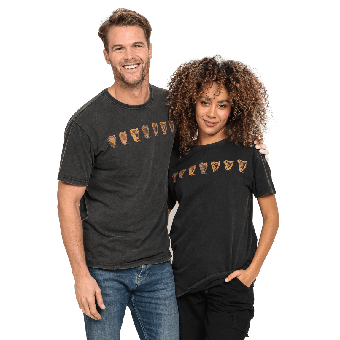 A man and woman stand close together, both wearing black Guinness Black Evolution Harp Premium Tees featuring a row of shark teeth. The man has his arm around the woman's shoulder, and they both have relaxed expressions. Their 100% cotton shirts perfectly complement their casual vibe.