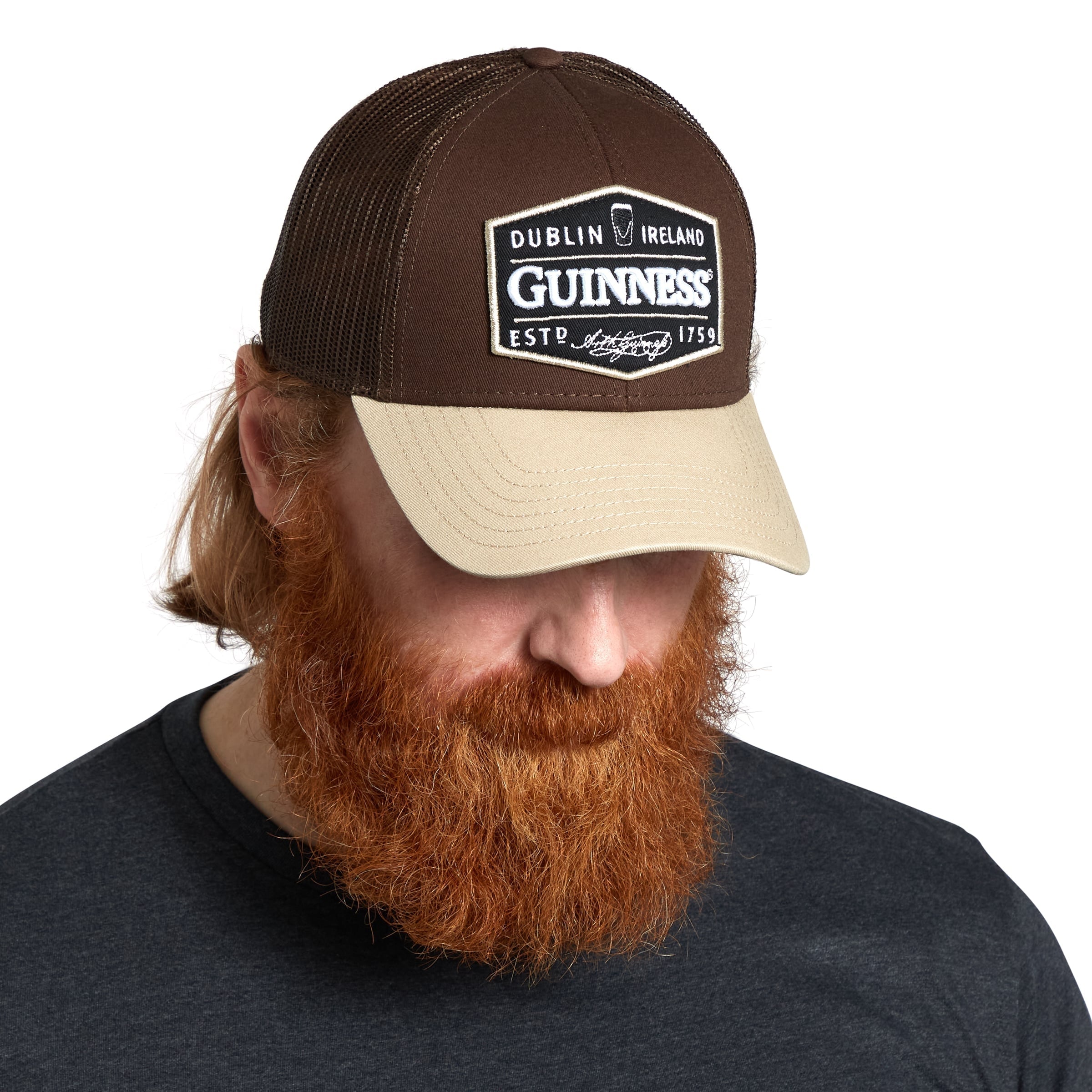 A man with a beard and red hair is wearing a Guinness Trucker Premium Brown with Embroidered Patch Cap.